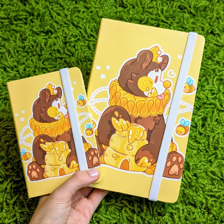 Adorable yellow leatherette sketchbook with a brown bear wearing a hat & ruff, eating honey from a beehive as bees fly all around.