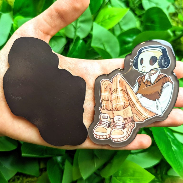 Front and back of a magnet with an aesthetic skeleton reclined and relaxed while listening to his favorite tunes.